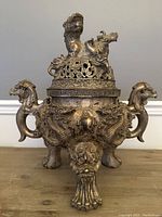 Full front view on tabletop showing tripod legs, dragon handles and lion‐top lid.