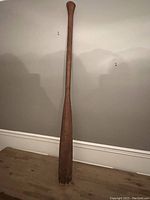 Full view of the 54-inch wooden canoe paddle leaning against wall, showing its long straight shaft, handle, and blade.