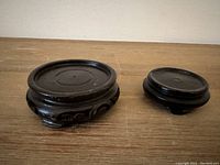 Two Chinese wooden stands for vases placed side by side on a wooden surface, showing their top surfaces and carved details visible on the larger stand.