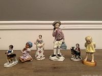 Front view of seven antique porcelain figurines showing varying sizes and details including children, adults, and animals.