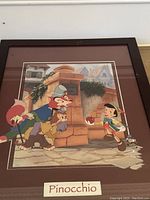 Framed Pinocchio art print showing characters including Pinocchio and two antagonists, a fox and a cat, in village setting.