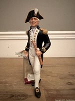 Front view of the Royal Doulton 'The Captain' figurine showing the captain in black and white naval uniform with gold buttons and epaulettes, standing beside a small table with nautical charts.