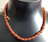 Front view of the amber bead necklace displayed on a black bust showing the beads' shape, color, and stringing material.