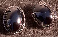 Close-up of both black stone oval earrings with silver-colored prong setting on dark background, front view.