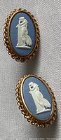 Pair of blue Wedgwood jasperware screw back earrings laid flat on fabric, showing front relief and gold-tone frames.