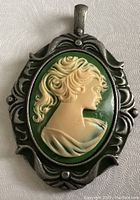 Front view of pendant showcasing detailed woman's profile cameo with green background and silver-tone ornate setting.