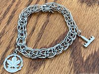 Photo of the full silver charm bracelet showing the chain weave and two attached charms on a wood surface.