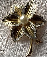 Close-up front view showing detailed damascene metal petals in gold and silver tones with a faux pearl in the center