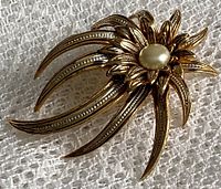 Close-up view of the Damascene flower brooch showing textured black and gold metalwork and faux pearl center.