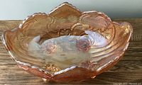 Side angle showing scalloped edge, embossed acorn design, and footed base of the carnival glass bowl.