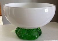 Side view showing white rounded bowl and thick green glass base with bubbles, placed on a table.
