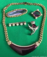 Top-down photo of the lot showing 4 distinct brooches and 16-inch necklace with purple enamel pendant and rhinestones on gold-tone chain.