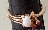Close-up of the ring showing the opal and two red stones set in gold-colored band.