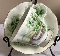 Teacup and saucer with shamrock pattern and scenic landscape, displayed on black stand