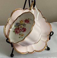 Teacup and saucer set displayed on a black stand showing the pink floral bouquet inside the teacup and scalloped edges with gold trim