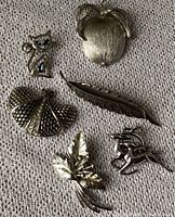 Six silver-coloured brooches on woven fabric: cat with blue eyes, apple, butterfly, feather, leaf, deer