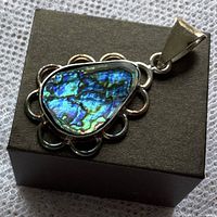 Close-up of teardrop-shaped sterling silver pendant with bright blue and green abalone shell veneer and scalloped silver border.
