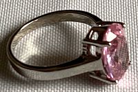 Side angle showing the silver-colored band and the prong setting holding the oval pink zirconia stone.