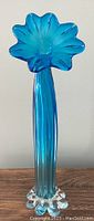 Full frontal photo of the tall blue glass vase showing the tapering body and flower bloom opening on top with clear bulbous base.