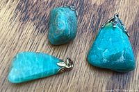 Photo showing three polished turquoise pendants on a wood surface, highlighting different shapes and metal bails.