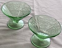 Two green depression uranium glass sherbet dishes showing overall shape and embossed pattern.