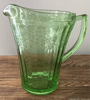 Side view of uranium green depression glass pitcher showing floral Cherry Blossom pattern and handle.