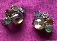 Close-up front view of one earring showing domed translucent central gem with outer rhinestones in green, brown, and blue colors on silver-tone metal.