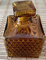 Top-down view of the square amber glass stopper of the decanter showing sunburst pattern and bubbles in glass.