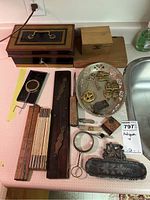 Wide view of assorted antique desk items including tin cash box, wood boxes, rulers, kaleidoscope toy, metal tray with brass desk pieces and magnifier.