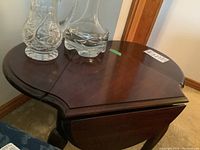 Angle showing the table with drop leafs partially extended and glass decanters placed on top (not included).