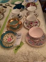 Photo showing eight assorted vintage cups and saucers including one marked Aynsley, with various floral patterns and gold accents.