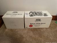 Photo of two white boxes labeled Heritage Village Collection Dickens' Village Series with Cobb Cottage and The Christmas Carol Cottage indicated on the boxes.