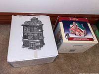 Two boxes of Department 56 lighted houses; the first is a white box with black illustration of 'The Flat of Ebenezer Scrooge', the second box is colorful with Dickensvale house artwork.