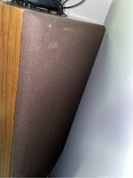 Side view of a Fidelio speaker showing wood veneer finish and brown fabric grill with minor marks.
