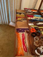 Wide shot showing multiple beaded necklaces in drawer and on dresser surface, orange, white, red, purple beads visible along with bangles.