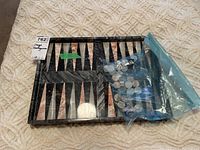 Onyx backgammon board folded open with plastic bag containing dice and discs on top, displayed on textured surface.