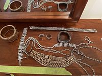 Full lot overview showing multiple rhinestone jewelry pieces arranged on a wooden surface in front of a mirror.