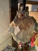 Figurine of a lady in a flowing yellow and white dress with pink accents inside a display case.