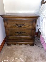 Side view of one wooden side table with two drawers and ornate handles, showing overall shape and some wear.