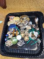 Top down view showing a variety of vintage clip-on earrings with different colors and styles laid out in a black tray.