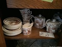 Photo showing five stacked espresso cups, six saucers in two piles, matching creamer, sugar bowl and part of a teapot, all with brown vintage transferware design on white china.