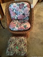 Wicker chair with floral cushions and non-matching storage footstool on carpeted floor.
