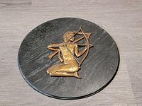 Full view of round black wood plaque with bronze Sagittarius archer, showing size and shape.