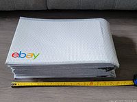 Stack of large white eBay branded padded bubble mailers with a yellow tape measure showing length about 14 inches