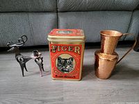 Full shot of three metal items: hammered copper jug, Tiger Chewing Tobacco tin, metal reindeer candle holder