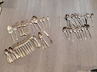 Overview of the flatware pieces laid on a wooden surface, showing silver plate pieces on the left and stainless steel pieces on the right.