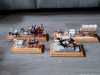Four built and painted horse-drawn wagons and stagecoach kits displayed on wooden bases, showing detailed paint and model work.