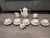 Full set displayed on floor with all pieces visible including cups, saucers, sugar bowl, pot with lid, and creamer. Shows size and arrangement.