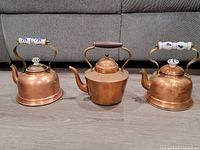 Group photo of three copper kettles showing front view with two ceramic Delft style handles and one wooden handle.