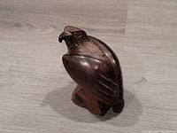 Front angled view showing bird shape, curved beak, feather details, and wooden base.
